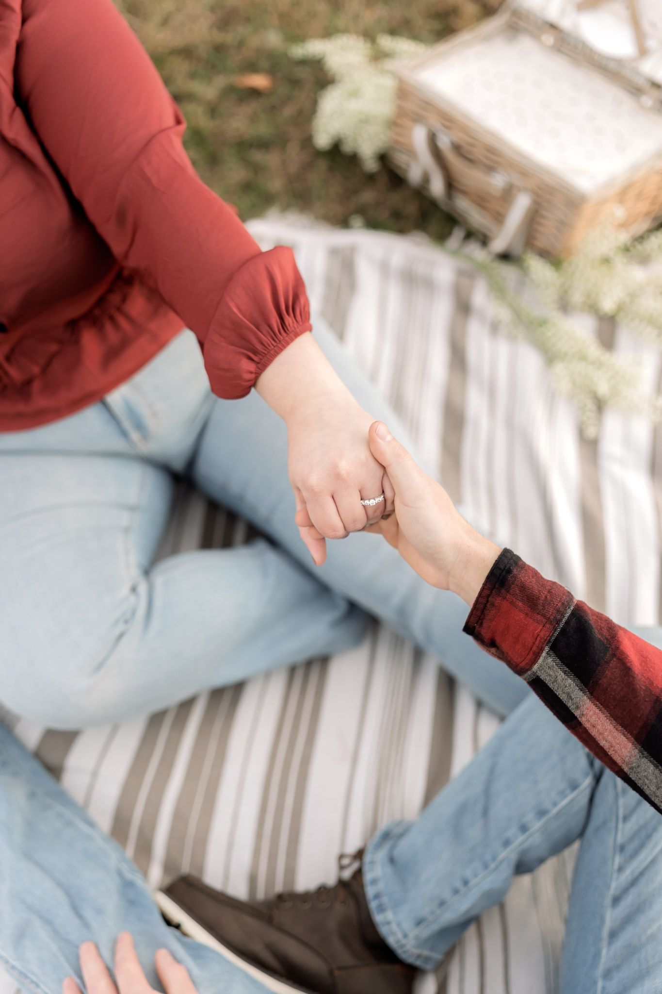 Close-up of hands touching while sitting on striped picnic blanket.