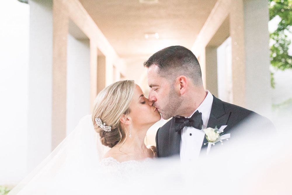 Intimate wedding portrait captured through white columns with soft focus edges.