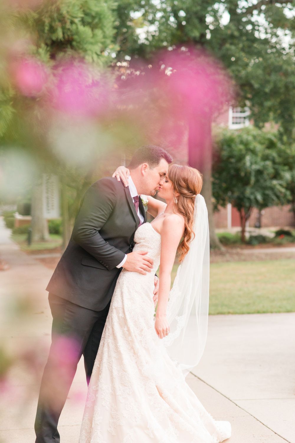 A romantic wedding portrait with soft pink bokeh effects in the foreground.