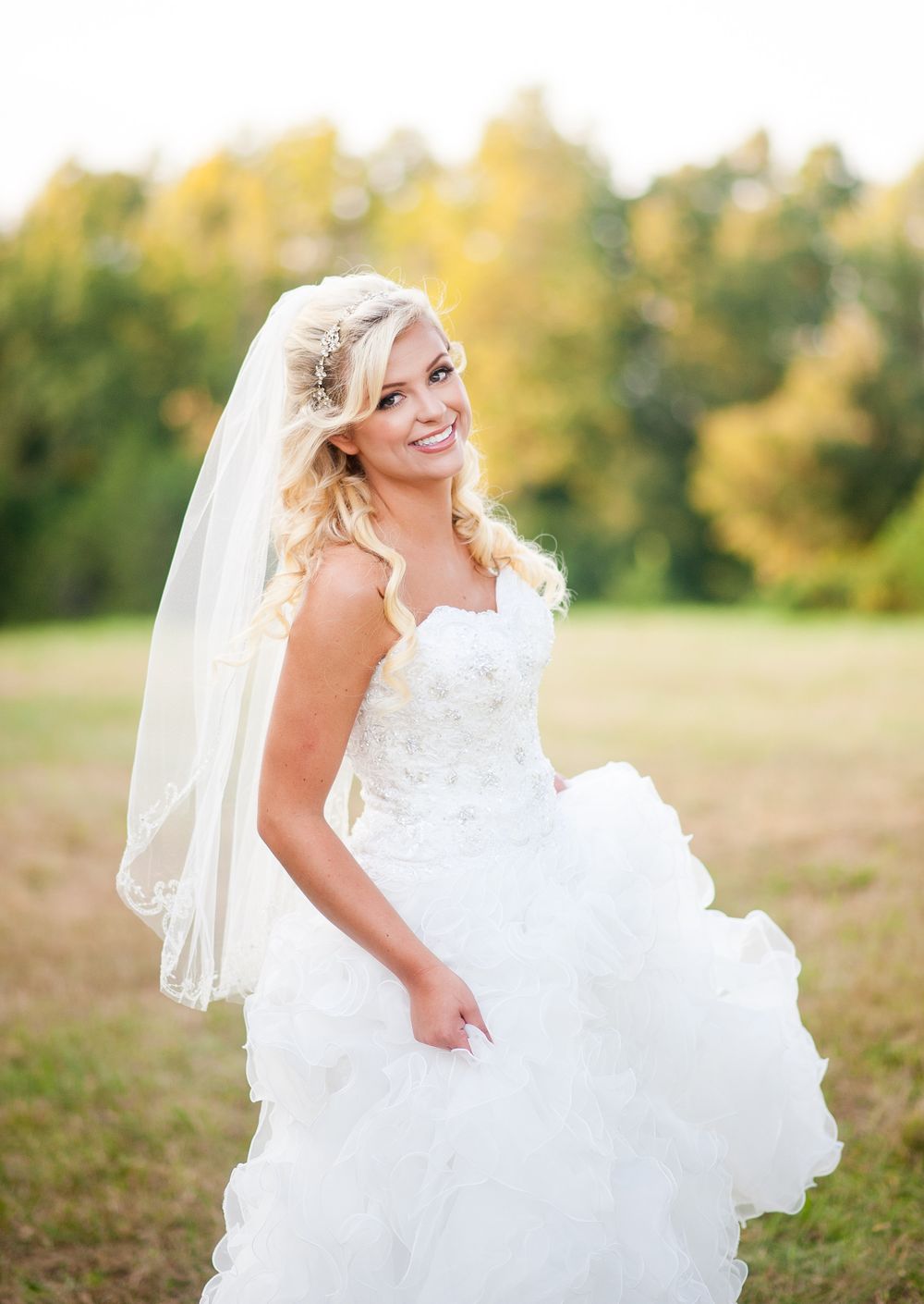 A bride in a flowing white gown poses outdoors against an autumn backdrop.