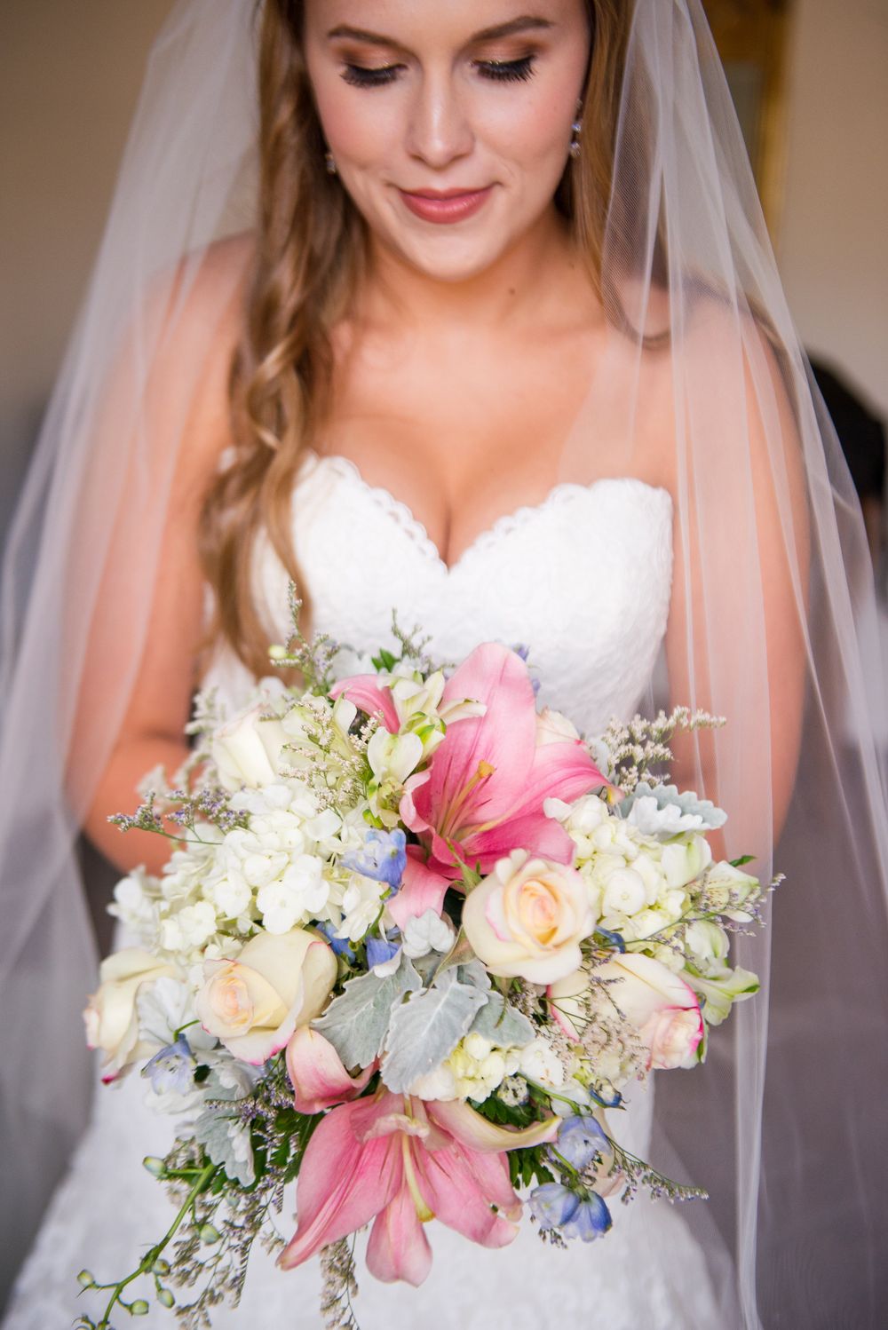 Close-up of bridal bouquet with pink lilies, roses, and delicate white flowers against white wedding dress.