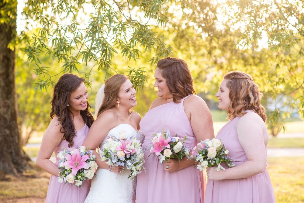 Bridesmaids in pink dresses share a joyful moment with the bride during an outdoor sunset photoshoot.