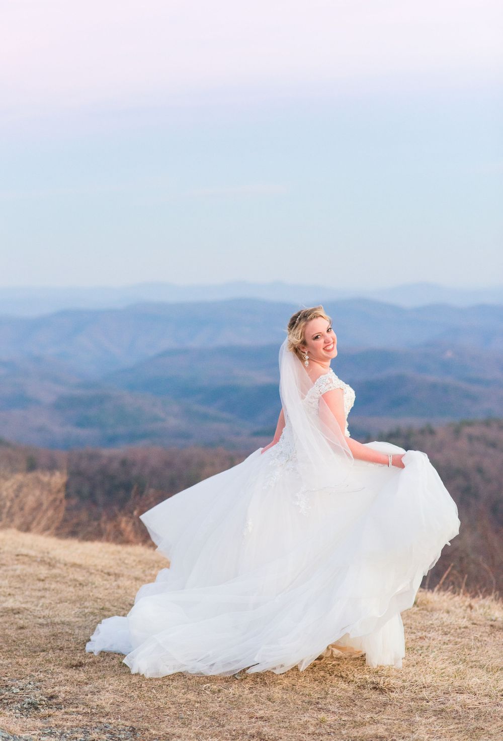 Flowing white wedding dress twirling against mountain landscape at sunset.