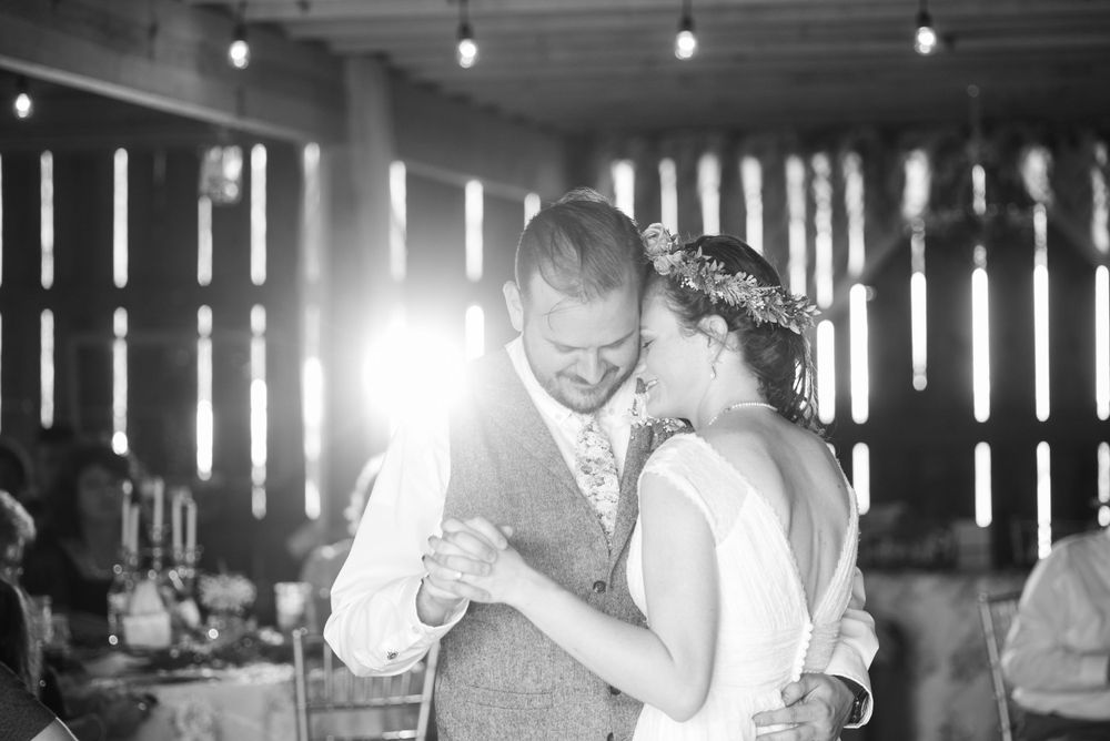 A romantic first dance moment captured in black and white in a rustic barn venue with dramatic lighting.