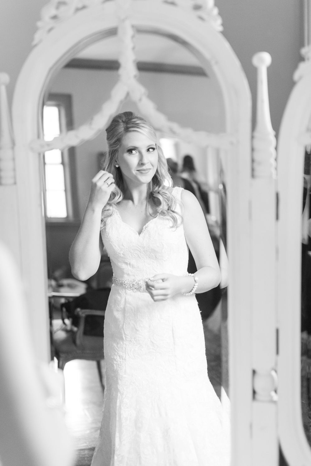 A bride in a lace gown stands elegantly framed by an ornate white archway.
