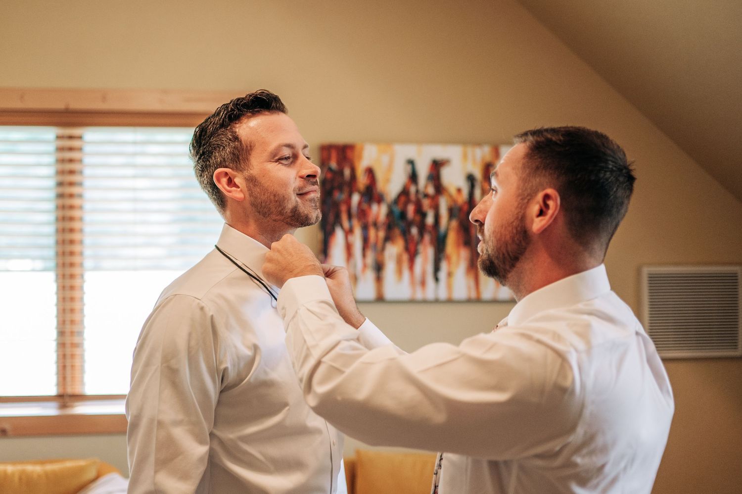 Two grooms helping each other get dressed for their wedding ceremony.