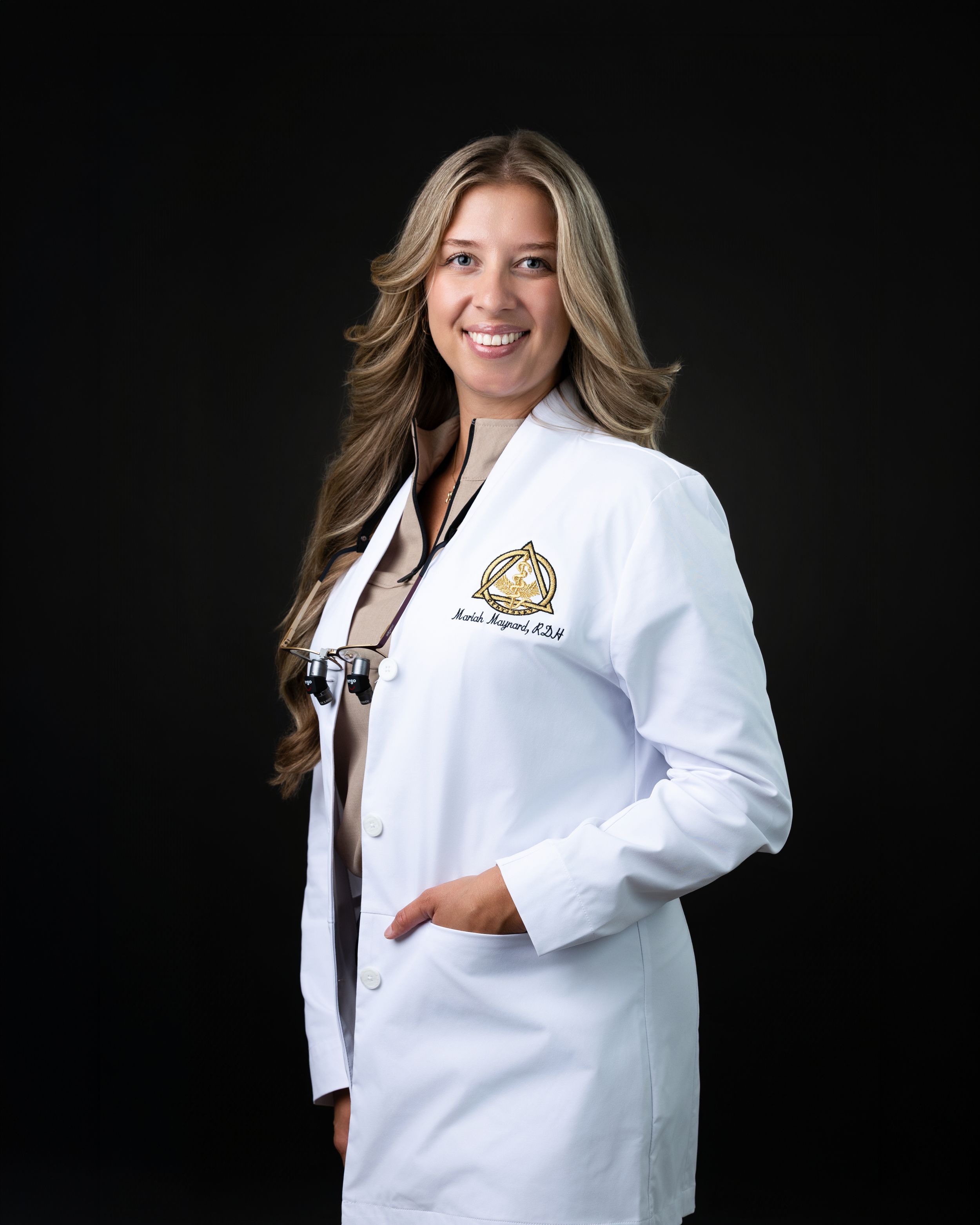 Smiling female doctor in white lab coat with stethoscope posing professionally against dark background.