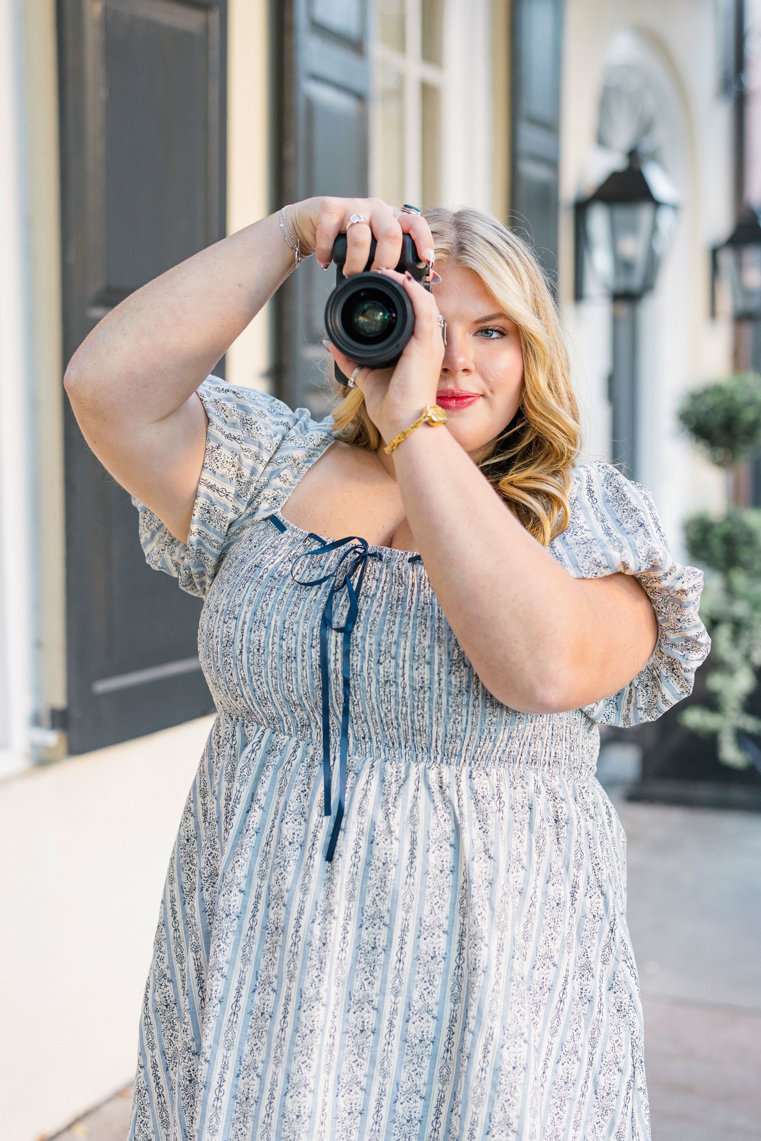Woman in floral dress demonstrates how to use a camera outdoors.