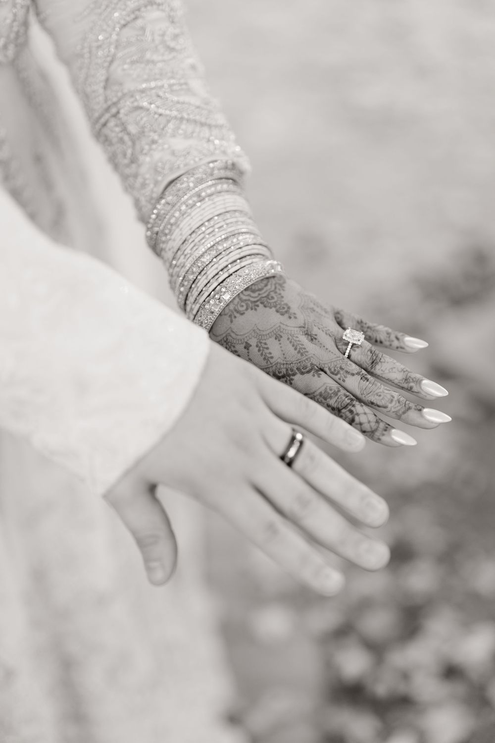 Black and white close-up of bride and groom hands showing wedding rings with intricate henna bridal art.