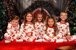 Children in matching red and white holiday pajamas pose together on a red blanket with festive decorations.