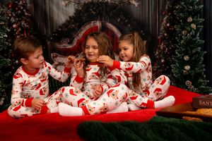 Children in matching red and white holiday pajamas play together on a red couch during Christmas.