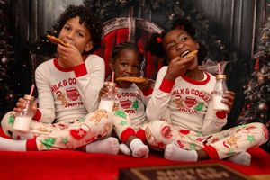 Children wearing matching holiday pajamas sit together on a couch during festive Christmas celebrations.
