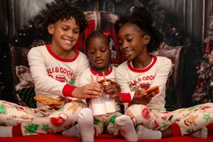 A group wearing matching holiday pajamas smiles while sitting together on a couch.