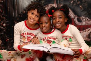 A group of people wearing matching holiday pajamas sit together on a couch near a Christmas tree.