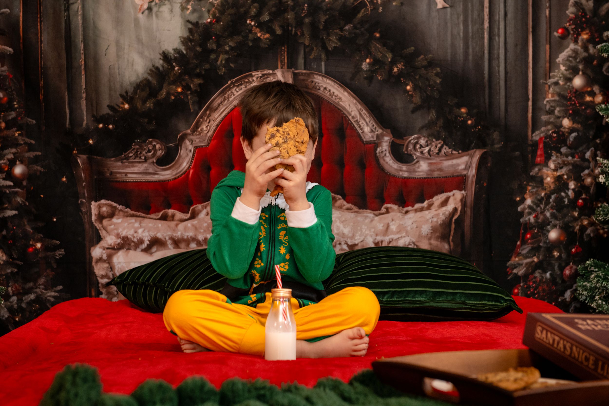 A person in a green sweater and yellow pants sits on a red couch surrounded by Christmas decorations.