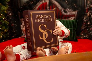 A hand flips through the pages of Santa's naughty and nice list book against a festive holiday background.