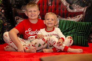 Two children in matching holiday pajamas pose together on a red blanket during a Christmas photo session.