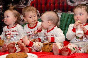 Group of babies in white bibs sitting at a table enjoying their first holiday meal together.