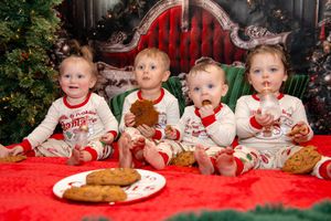Children in matching holiday pajamas sit together on red blankets during a Christmas photo session.