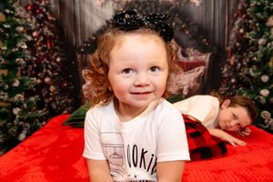 A child lies on a red blanket surrounded by holiday decorations and twinkling Christmas lights.