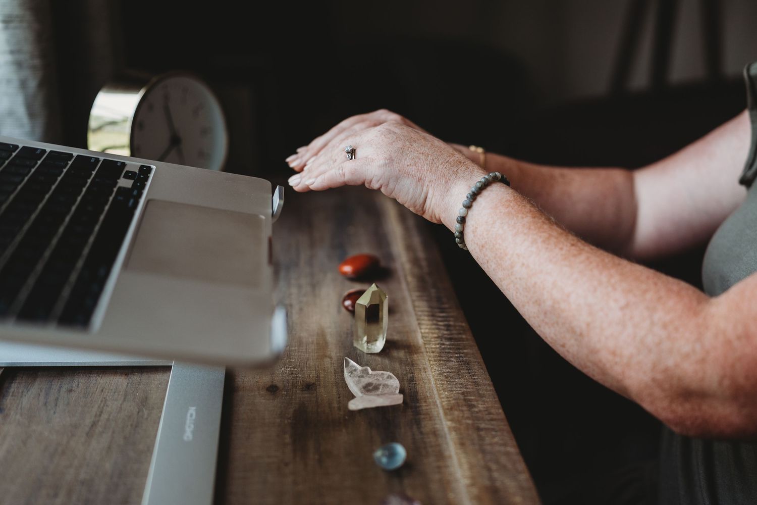 Person's hand reaching across wooden desk with laptop and small objects in workspace setting.