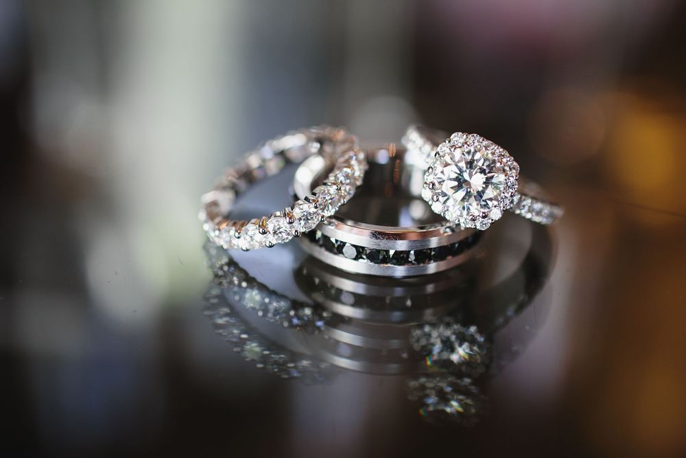 A close-up view of a sparkling diamond engagement ring with a detailed band against a dark background.