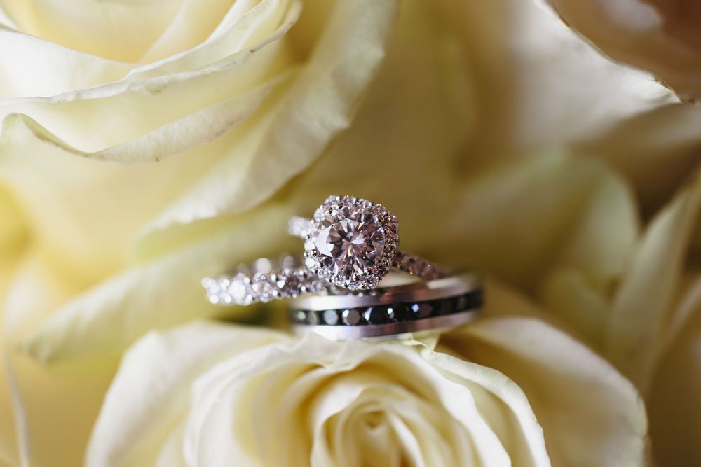 Close-up view of delicate white rose petals with sparkling diamond rings nestled among the soft floral textures.