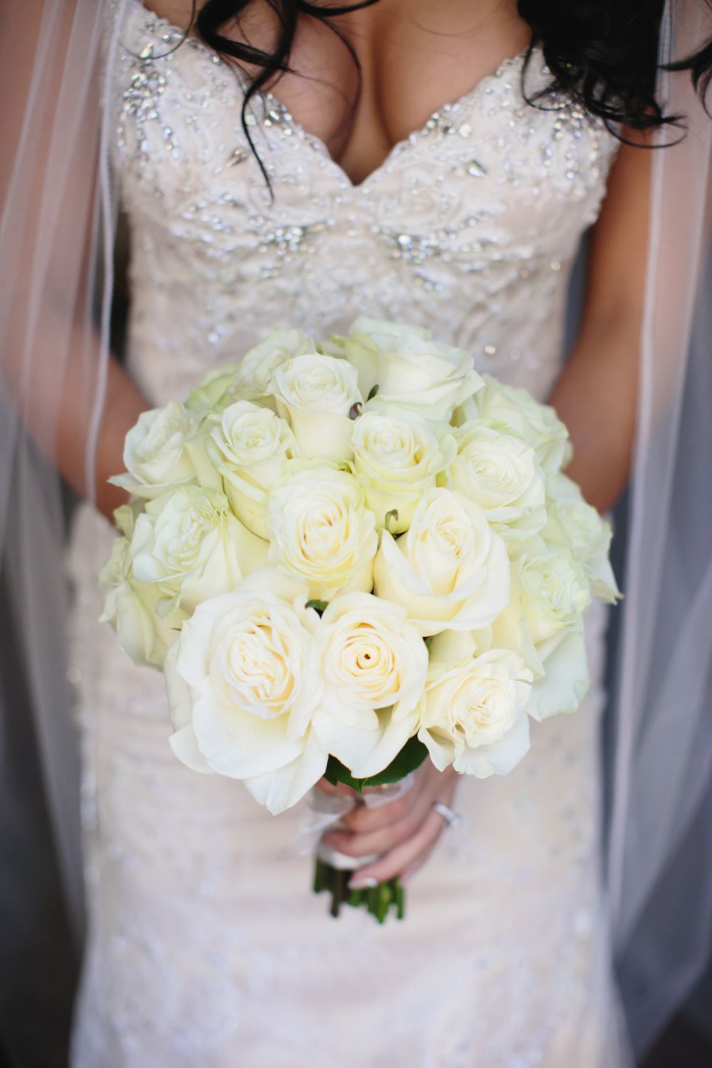 Close-up shots of an elegant white rose wedding bouquet held against a lace wedding dress.