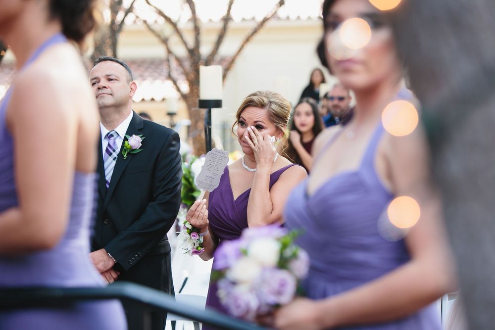 Wedding guests and attendants in purple dresses gather during an outdoor celebration.