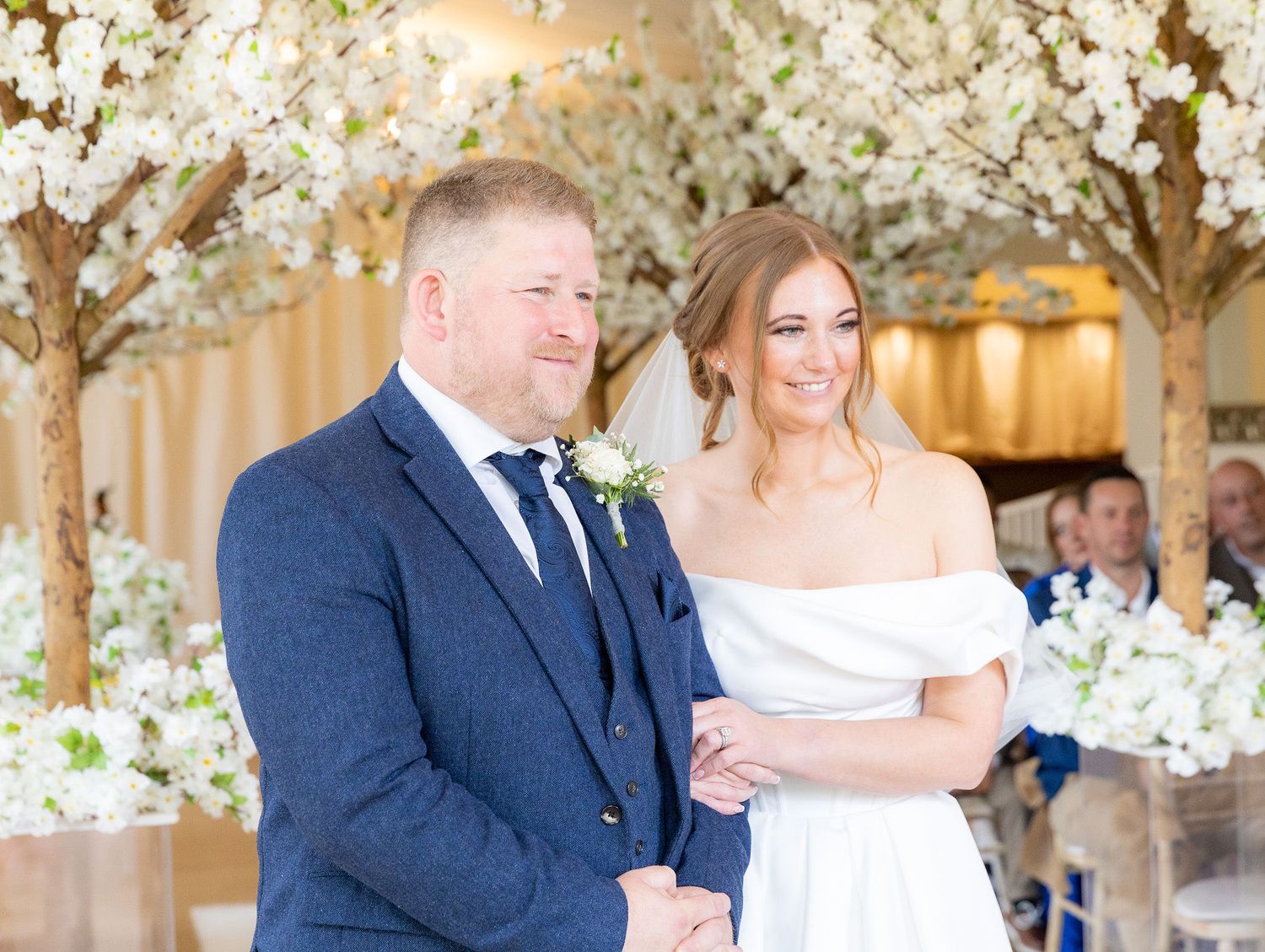 Wedding couple shares romantic moments under white floral decorations in elegant indoor venue.