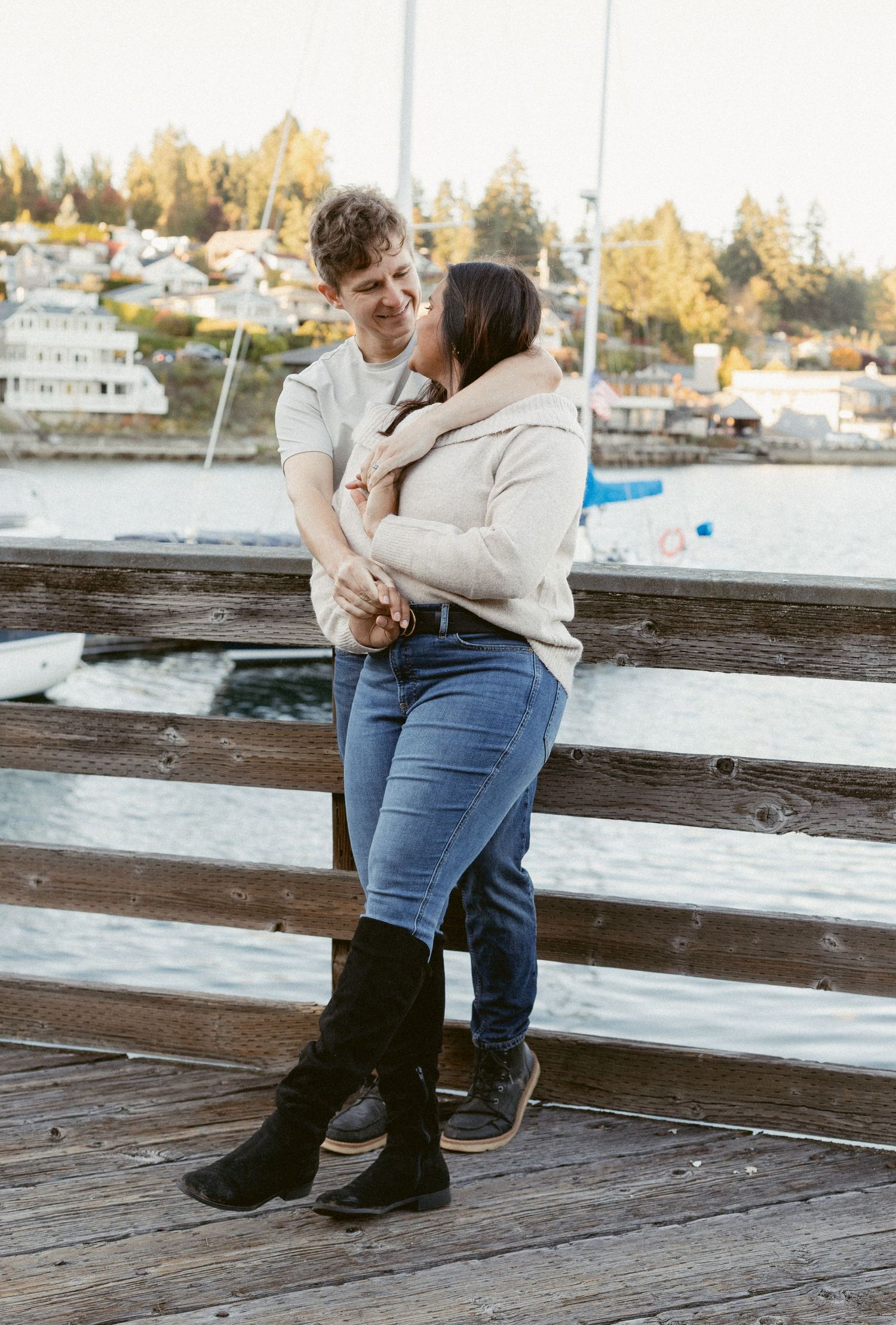 A couple sits together on a wooden dock overlooking a waterfront during golden hour.