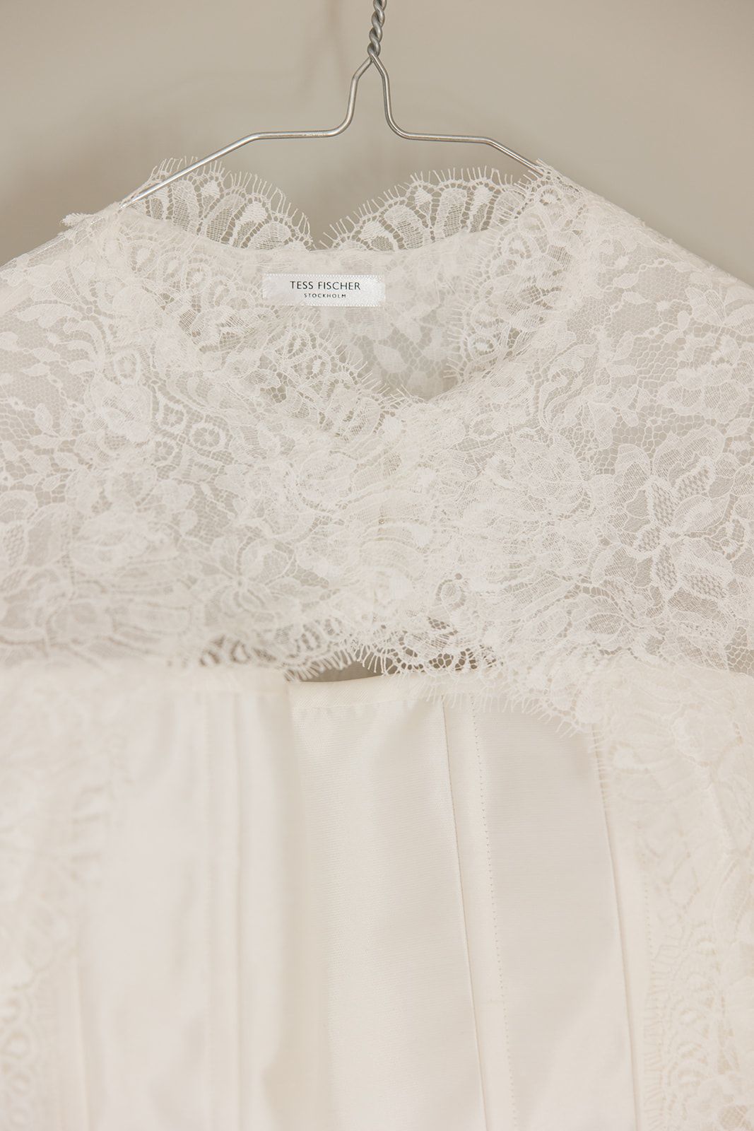 White lace wedding dress bodice with delicate floral pattern hanging on display against neutral background.