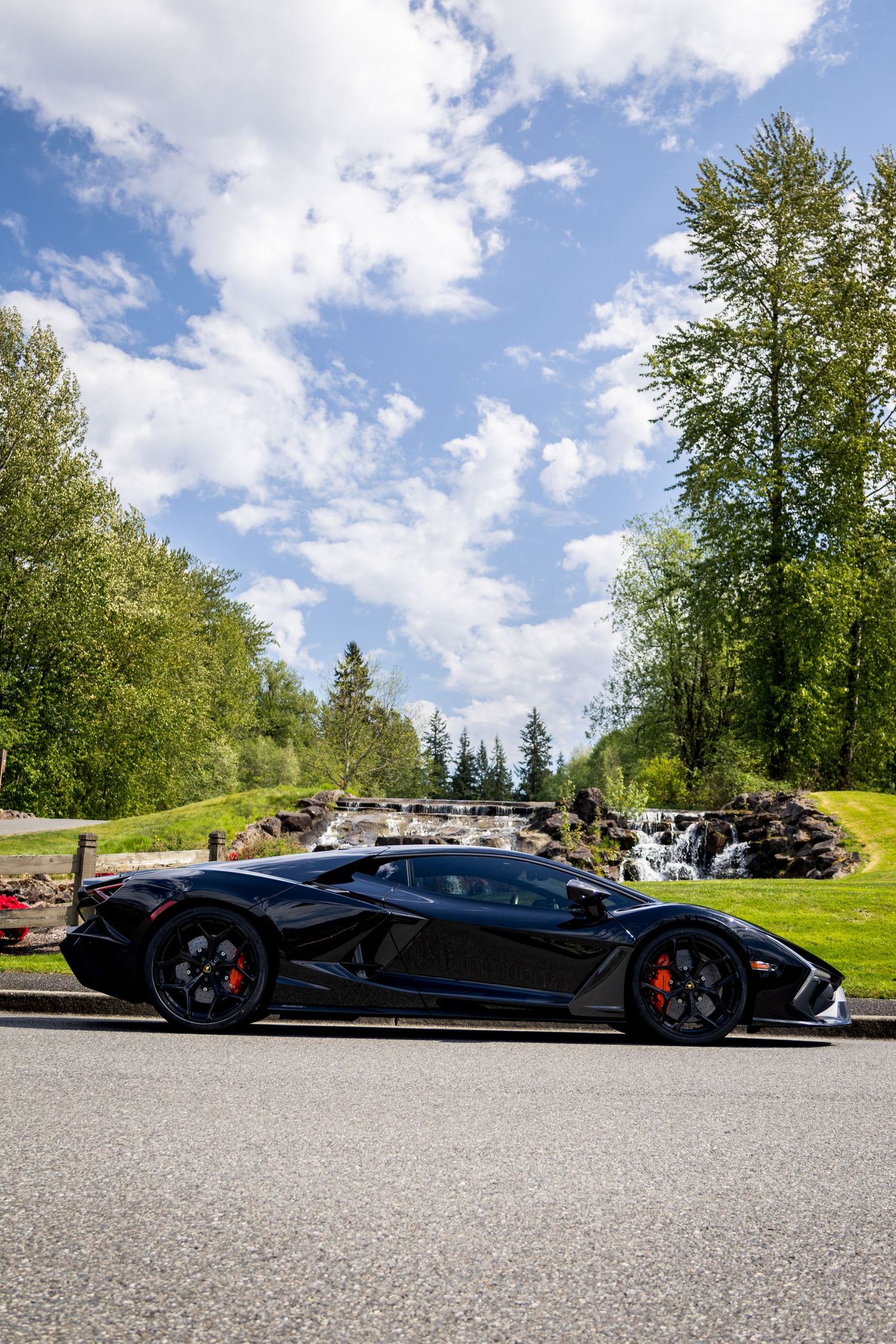 Black luxury sports car photographed from multiple angles on a sunny day against trees and blue sky background.