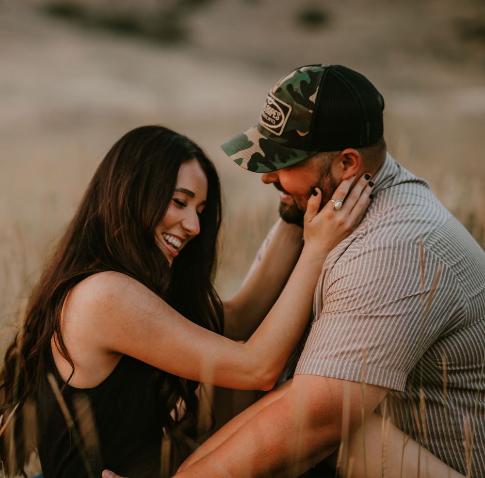 Intimate candid moment between couple sharing laughter and affection during golden hour photo session outdoors.