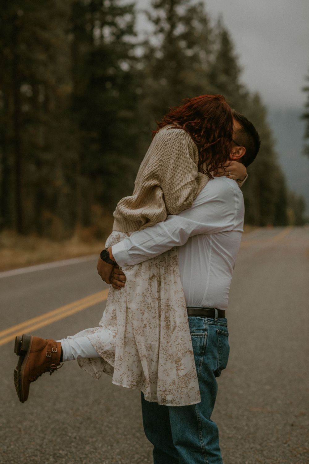A romantic couple embraces and spins on an empty mountain road during golden hour in autumn.