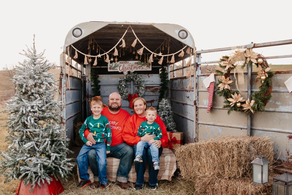 A rustic Christmas photo setup in a barn with a festive tree, hay bales, and decorative lights.