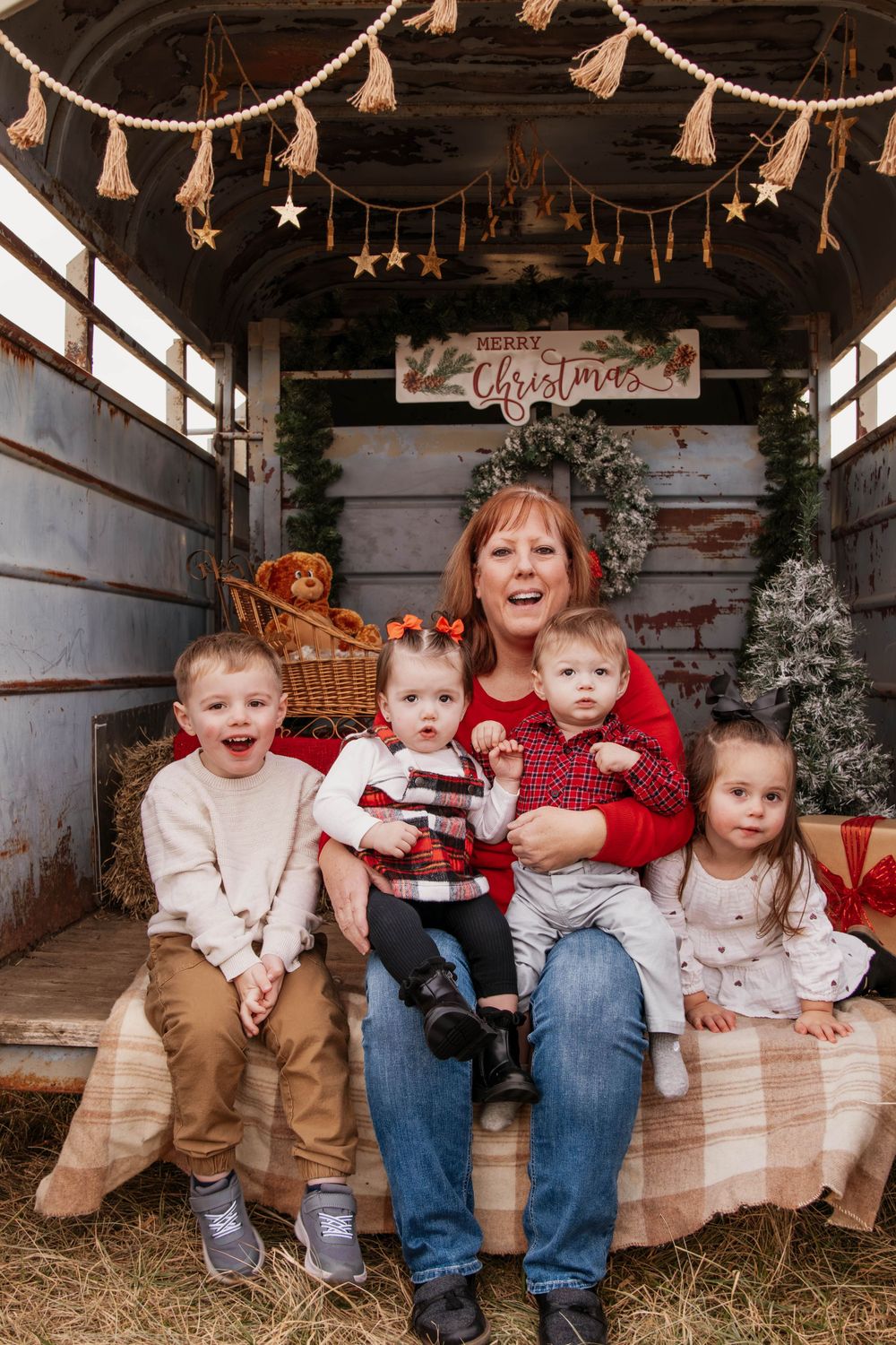 Children and adults share joyful holiday moments in a decorated rustic trailer with tasseled garland.