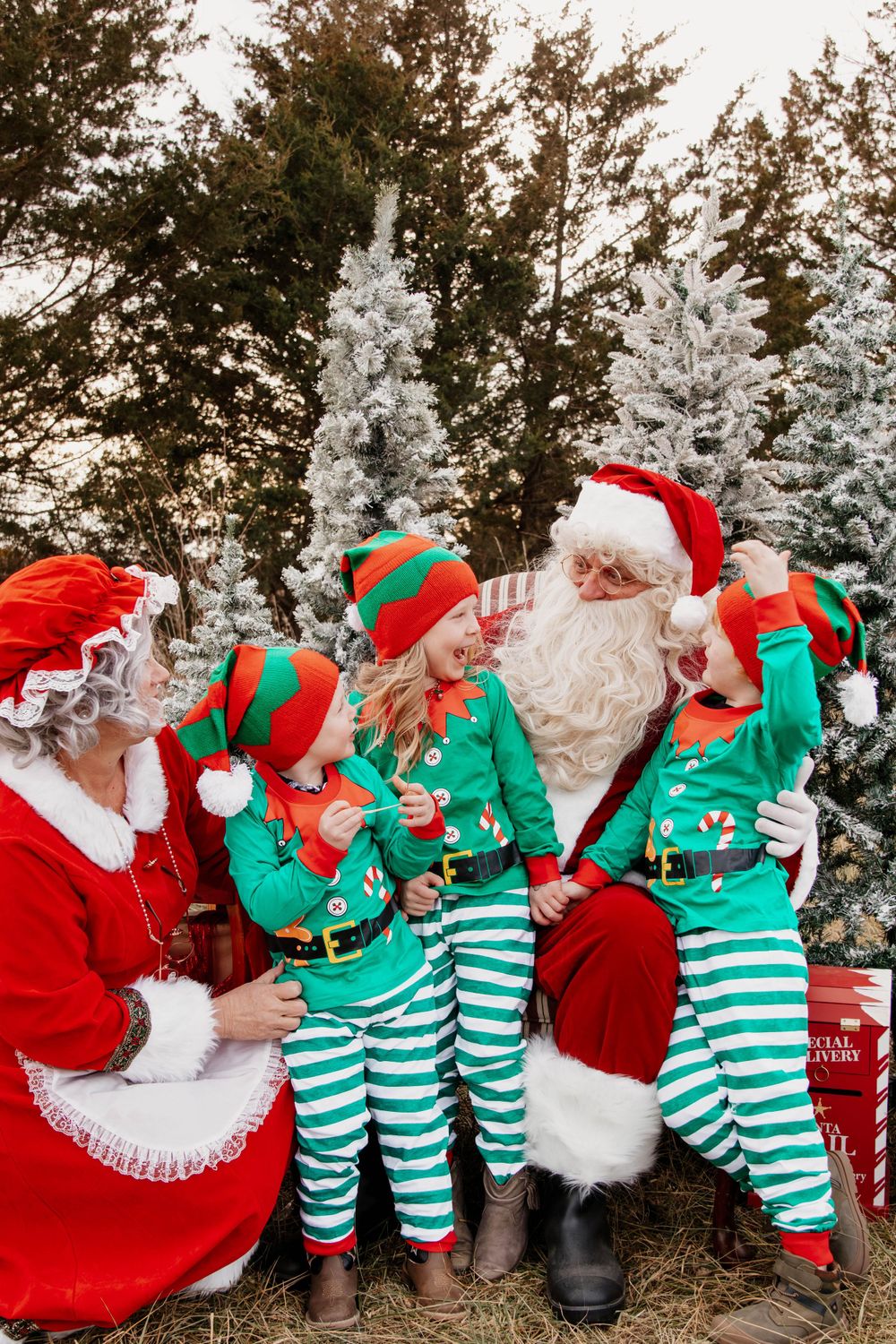 Holiday characters in red and green striped outfits pose together in front of snow-covered trees.