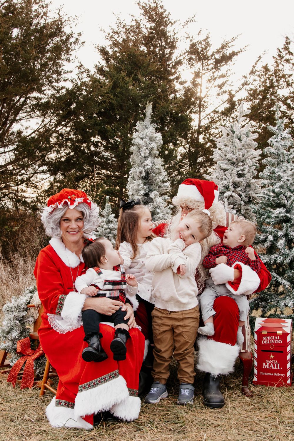 A joyful holiday gathering with traditional costumes against snow-covered trees and red gift boxes.
