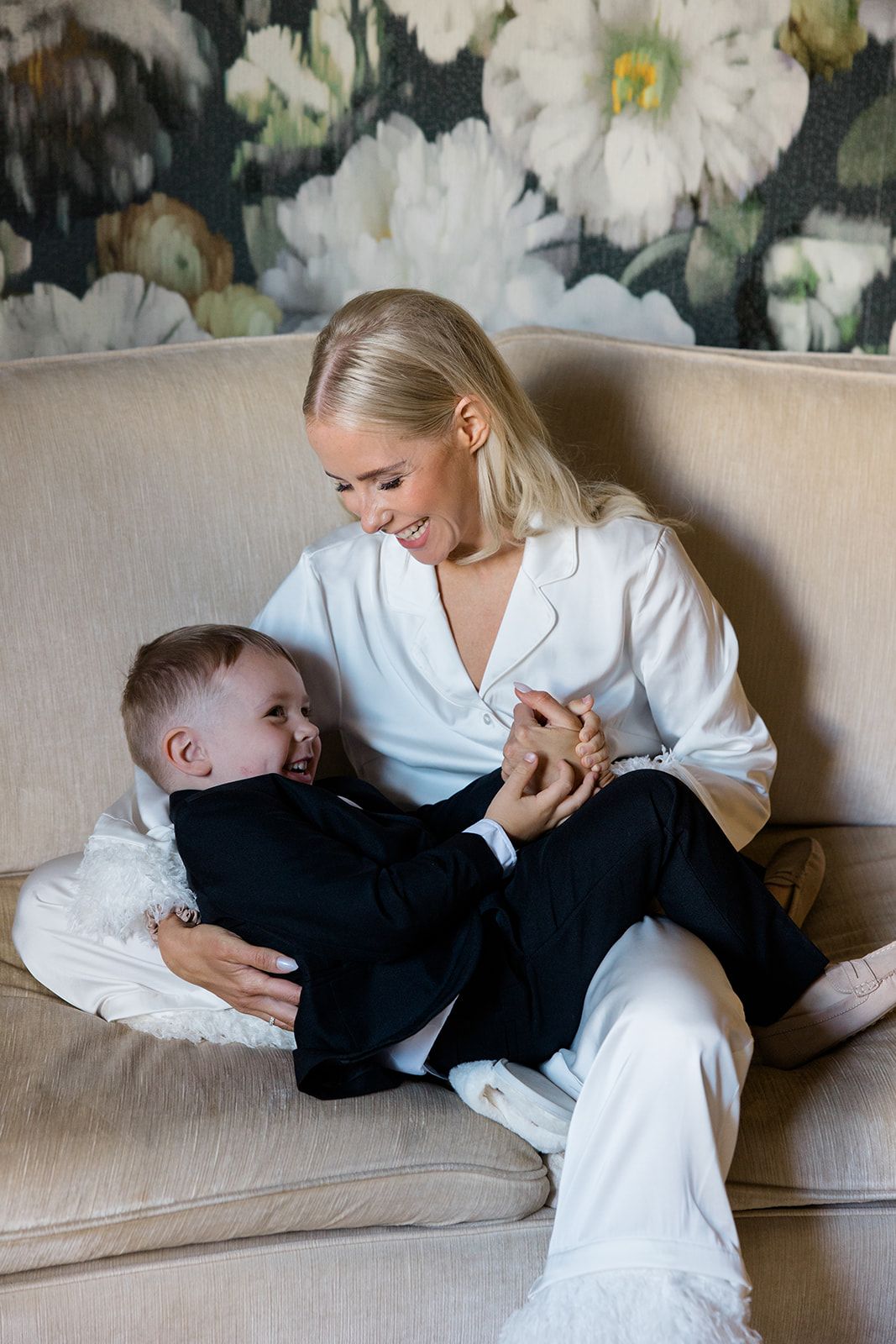 A tender moment shared between parent and child lounging together on a beige couch in white clothing.