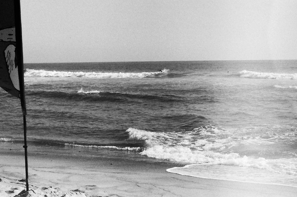 A panoramic black and white photograph of waves crashing on a rocky beach with dramatic ocean surf and coastline.
