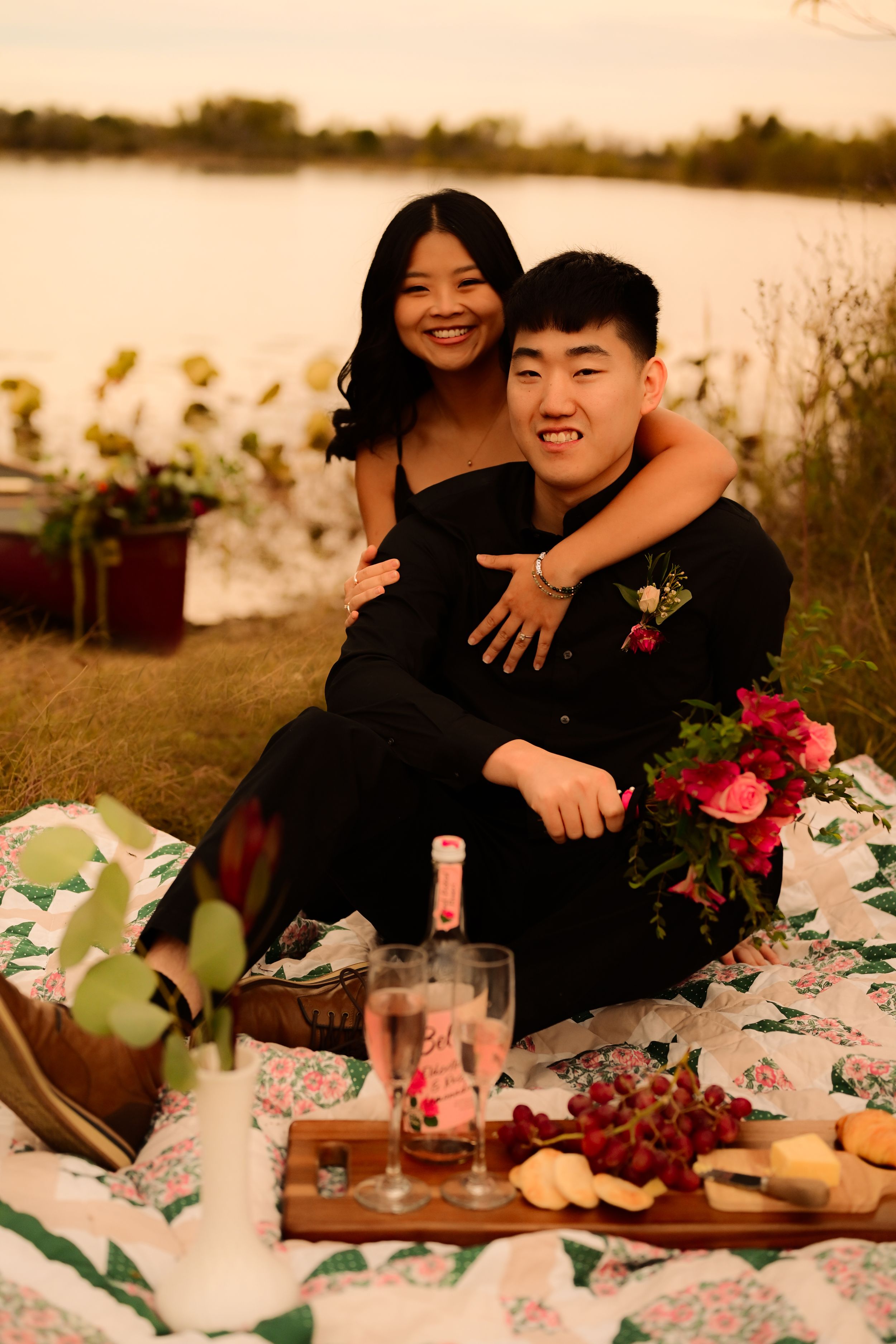A romantic picnic setup at sunset with flowers, wine glasses, and a charcuterie board laid out on a blanket.