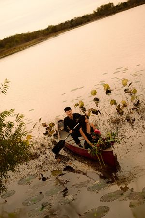 A couple paddling in a red canoe through lily pads on a serene lake at golden hour.