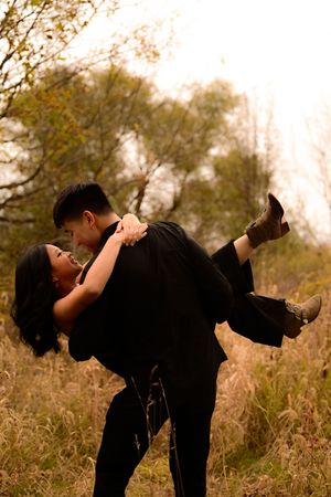 A romantic couple in black outfits sharing intimate moments in a golden field at sunset.