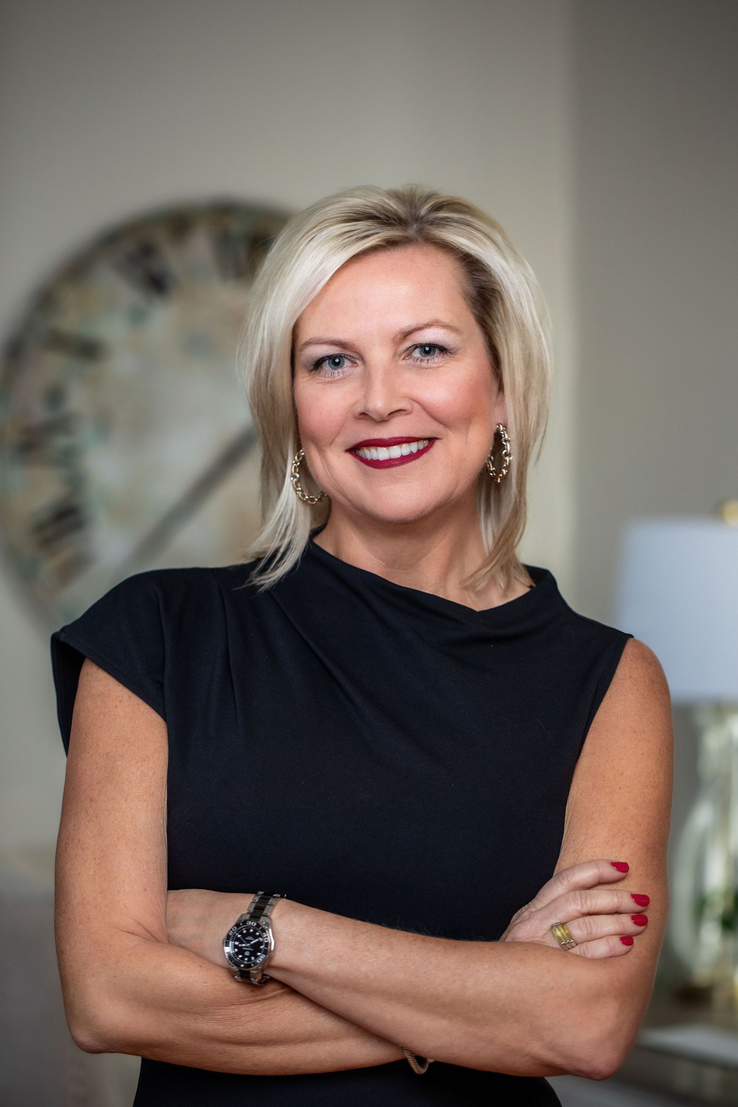 Smiling person in a navy blue sweater sitting casually on a chair against a dark background wearing an Apple Watch.