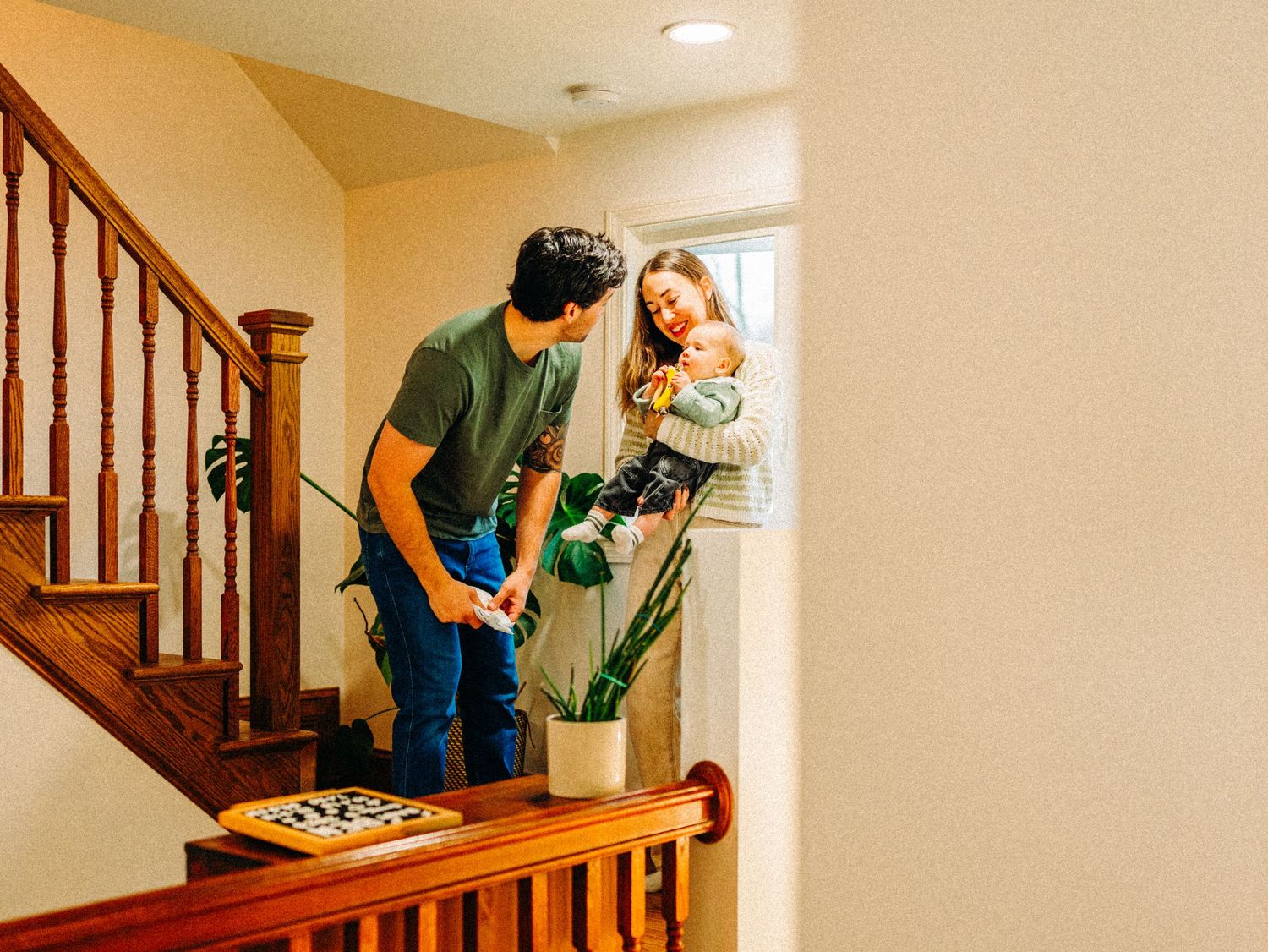 Two people work together to carefully carry a heavy dresser up a carpeted staircase in a home.