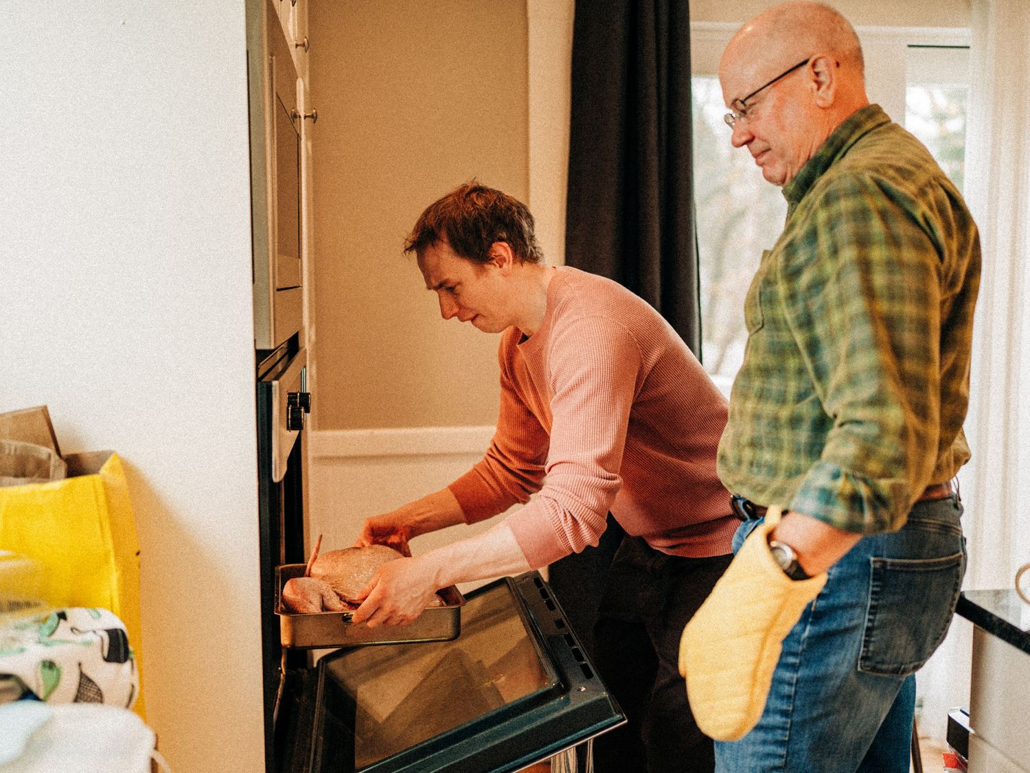 Two people work together in a kitchen while preparing food at a counter near a window.