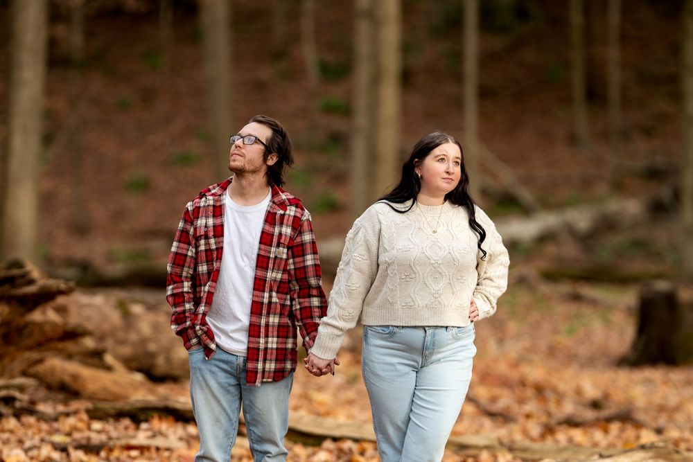 Couple holding hands while strolling through an autumn forest with fallen leaves.