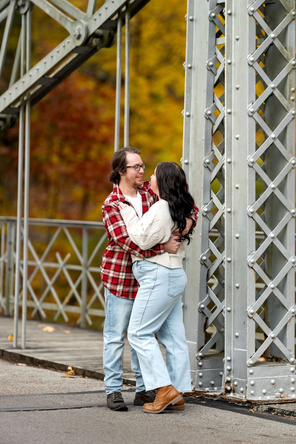 Romantic couple embracing and kissing by a metal bridge structure in autumn.