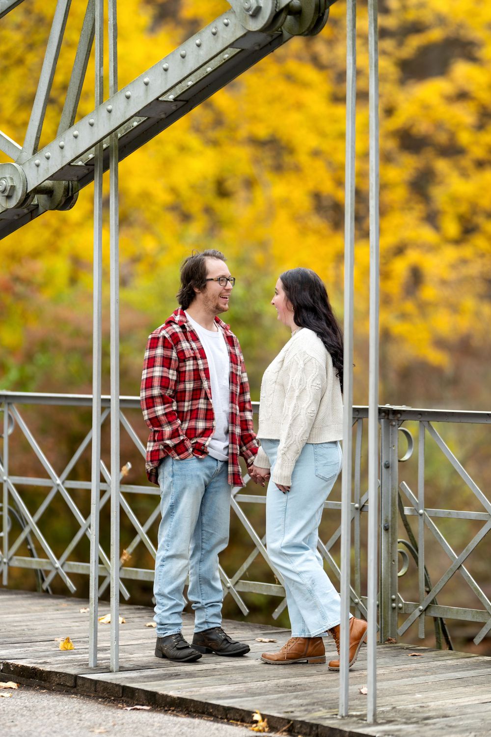 Couple holding hands on a wooden bridge with bright yellow autumn leaves behind them.